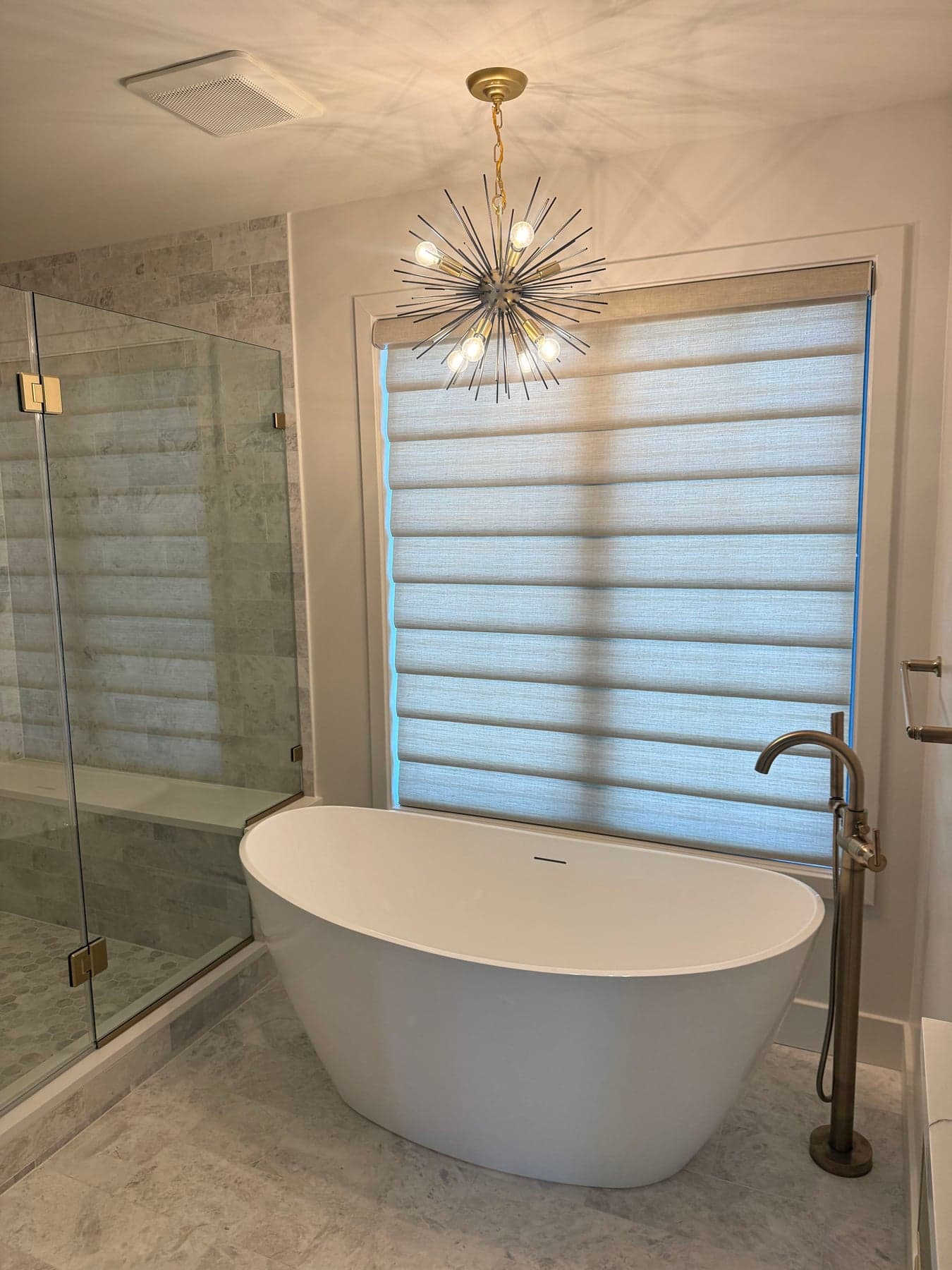 Light-filtering roman shade above a freestanding soaker tub in a primary bath
