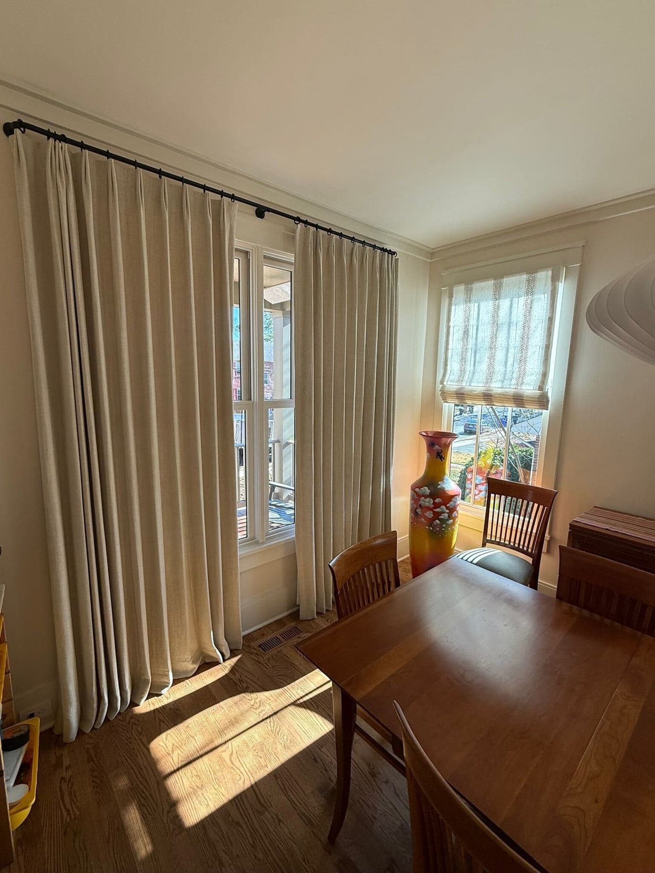 Pinch-pleat linen drapery panels with a striped roman shade on corner windows in a dining room