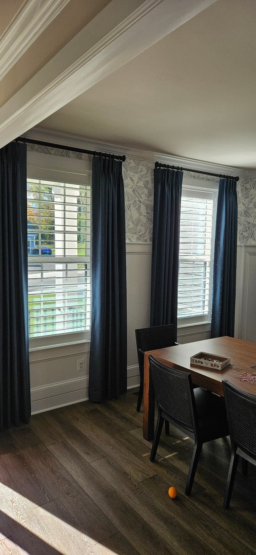 Navy pinch-pleat drapery panels framing two windows in a wallpapered dining room