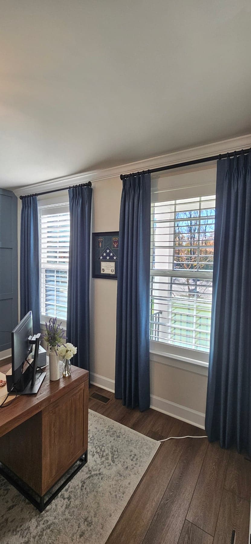 Navy pinch-pleat drapery panels over white blinds in a home office