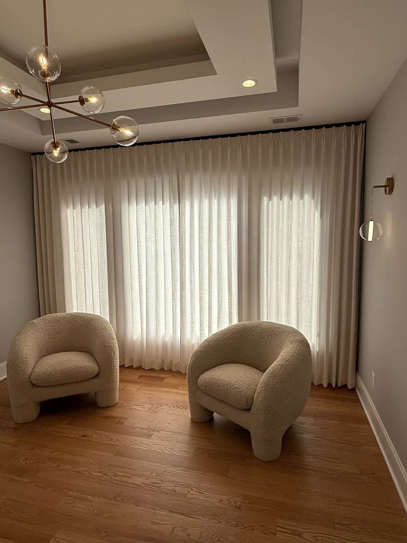 Wall-to-wall sheer pinch-pleat drapery glowing with daylight in a sitting room